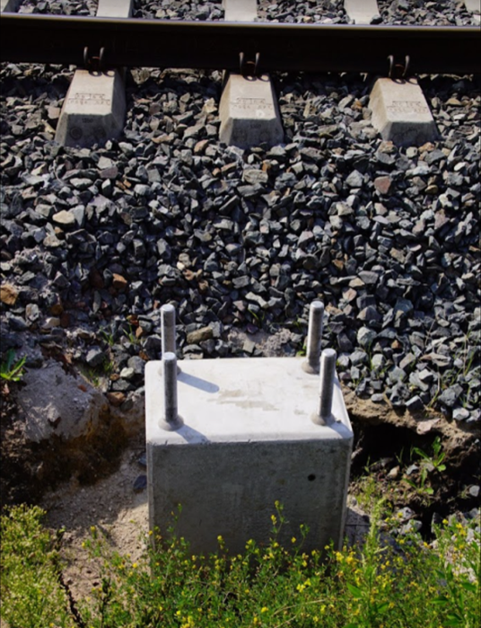 Ilustracja przedstawia betonowy fundament palowy, z którego wystają cztery stalowe pręty. 