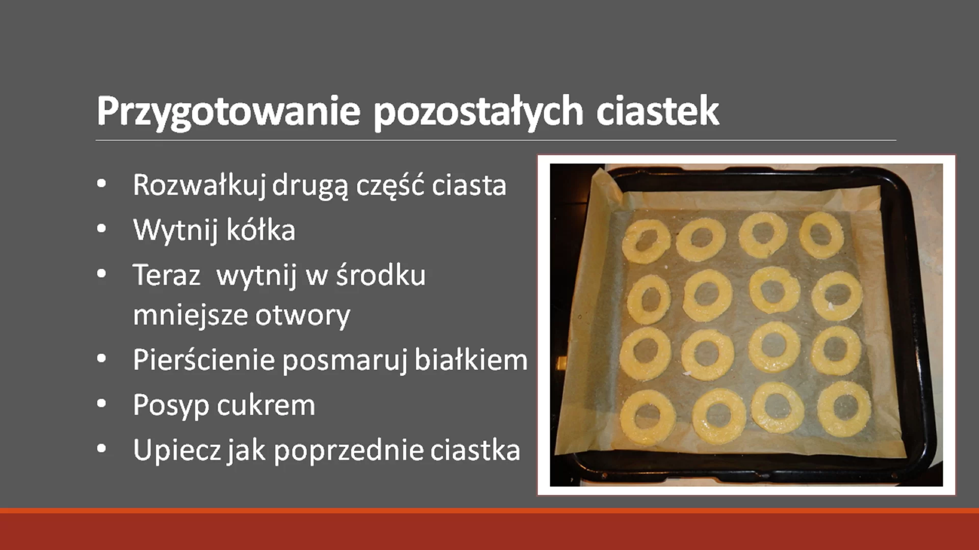 Piąty slajd pod tytułem: "Przygotowanie pozostałych ciastek". Tytuł ma pogrubioną i większą czcionkę. Pod nim znajduje się tekst: "Rozwałkuj drugą część ciasta. Wytnij kółka. Teraz wytnij w środku mniejsze otwory. Pierścienie posmaruj białkiem. Posyp cukrem. Upiecz jak poprzednie ciastka.". Tekst jest napisany w punktach. Obok niego, po prawej stronie znajduje się zdjęcie w ramce przedstawiające ciasteczka z otworami rozłożone na blaszce wyłożonej papierem do pieczenia.