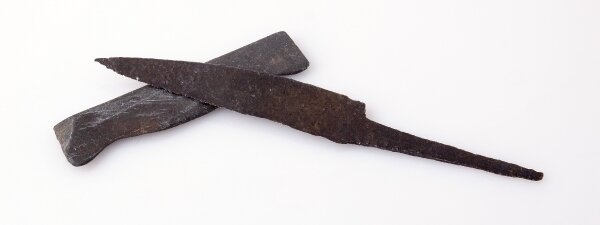 Ilustracja przedstawia nóż żelazny wraz z narzędziem do jego ostrzenia, czyli osełką. Nóż ma szerokie ostrze, następnie węższy trzonek do trzymania. Osełka ma kształt niewielkiego prostokąta.   