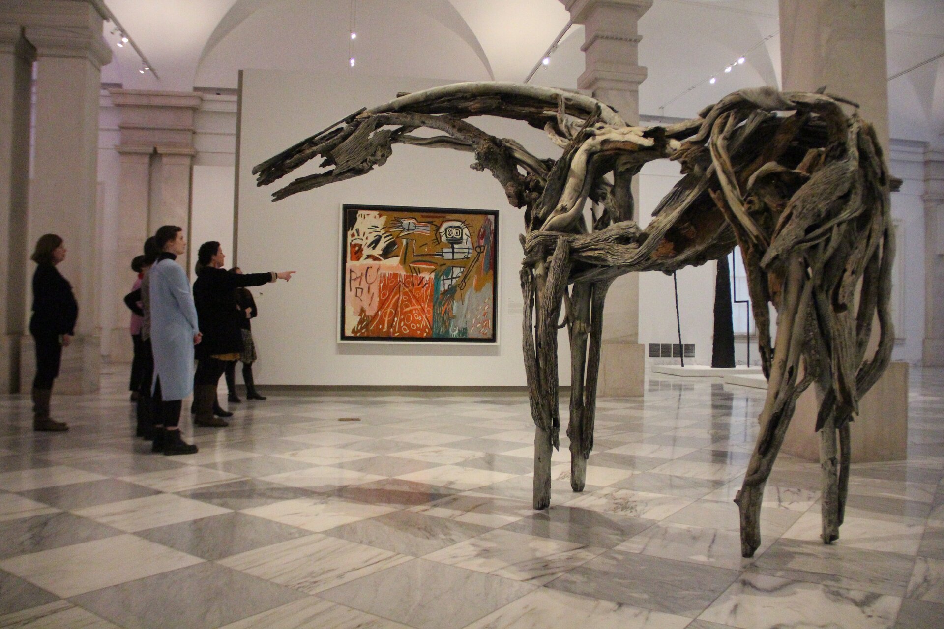 Ilustracja przedstawia fotografię Deborah Butterfield pod tytułem: „Monekana”. Na zdjęciu znajduje się galeria sztuki. Po lewej stronie przedstawionych jest siedem postaci. Są to obserwatorzy dzieł sztuki. Jedna z postaci ma wyciągnięta rękę w kierunku dzieła sztuki, znajdującego się po prawej stronie. Kompozycja przedstawiona po prawej stronie, przedstawia zwierzę, przypominające konia. Ma cztery nogi, ogon, długą szyję oraz głowę. Na środku jasnej ściany galerii znajduje się obraz. 