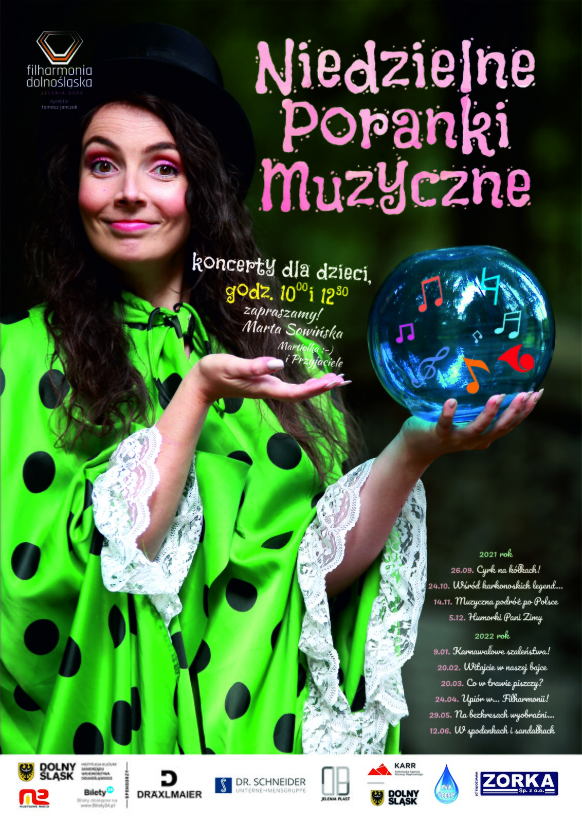 Zdjęcie przedstawia plakat promujący Niedzielne Poranki Muzyczne. Po prawej stronie znajduje się kobieta ubrana w zielony płaszcz w czarne groszki. W lewej ręce trzyma szklaną kulę z czerwonymi nutami. Kobieta ma czarne, długie włosy. W lewym górnym rogu znajduje się napis „filharmonia dolnośląska”. 