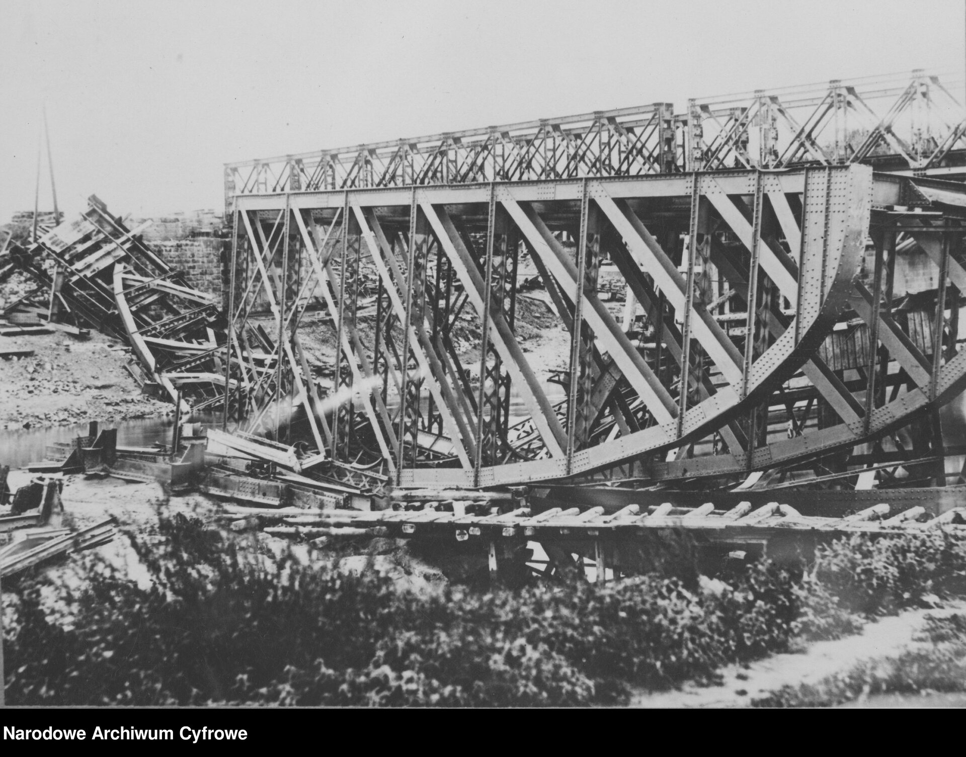 Zdjęcie przedstawia zniszczony most kolejowy nad rzeką.