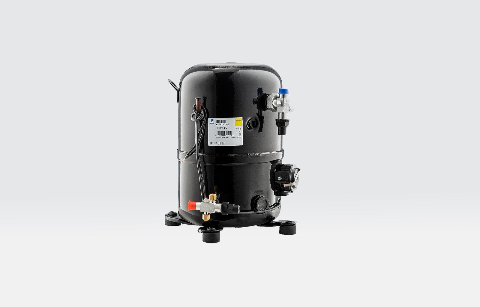 Na zamieszczonym zdjęciu przedstawiona jest sprężarka hermetyczna, która charakteryzuje się cylindrycznym kształtem z zaokrągloną kopułą w części górnej oraz nóżkami umożliwiającymi stabilne postawienie urządzenia. Na zewnętrznej obudowie sprężarki widoczny jest kabel zasilający oraz dwie rurki zakończone zaworami.