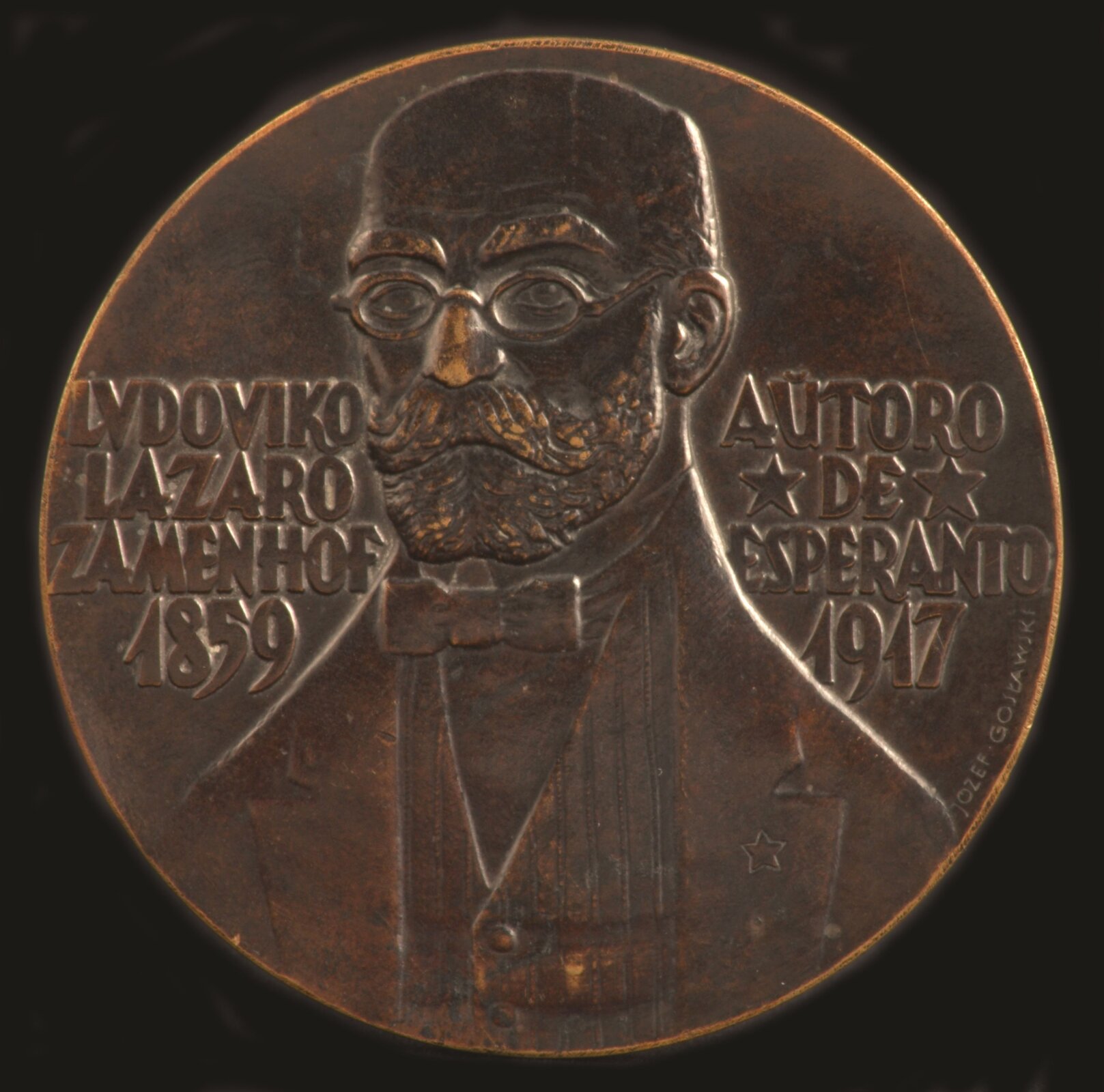 Ilustracja przedstawia medalion Józefa Gosławskiego pt.: „Medal z Ludwikiem Zamenhofem”. Na ilustracji widoczny jest medal z podobizną Ludwika Zamenhofa. Medal jest  okrągły i brązowy. Obok podobizny Ludwika Zamenhofa wypisane są jego imię, nazwisko oraz data urodzin i śmierci .