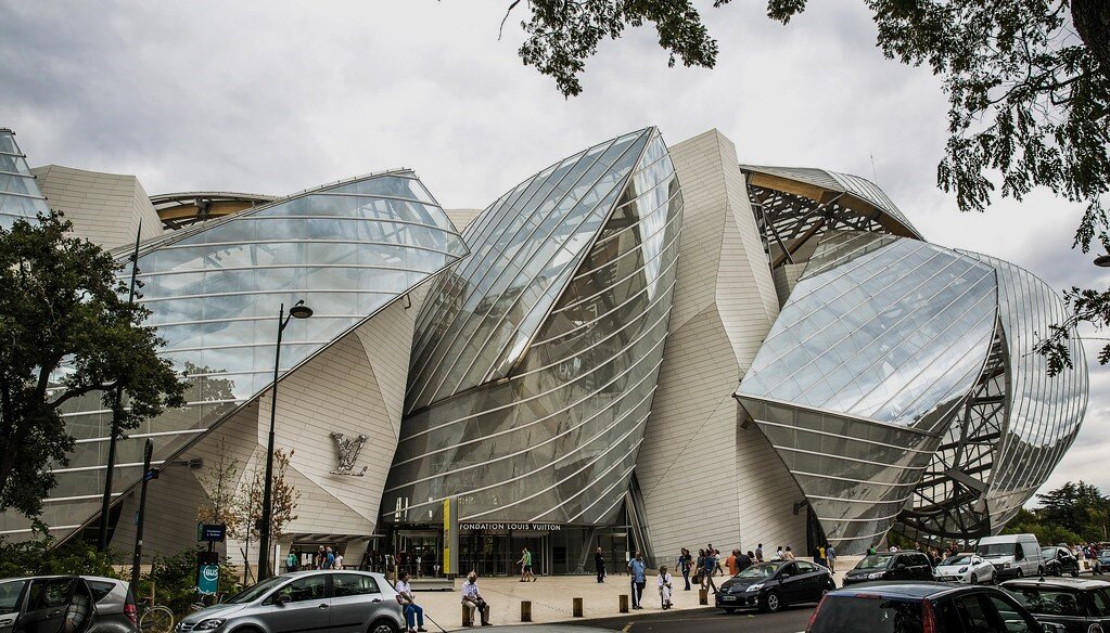 Budynek Fundacji Louisa Vuitton (czyt. luisa vitą), sławnego projektanta mody w Paryżu jest wyjątkowym przykładem odważnej, nowoczesnej formy w architekturze. Składa się z kilku nieregularnych, jakby pogiętych brył. Zbudowany jest ze szkła, betonu oraz metalu, które raz odbijają, to znów przepuszczają i zatrzymują światło. Nieregularne bryły budowli ułożone są jedna obok drugiej. Przed budynkiem stoją ludzie, zaparkowano kilka samochodów. Po bokach rosną drzewa.