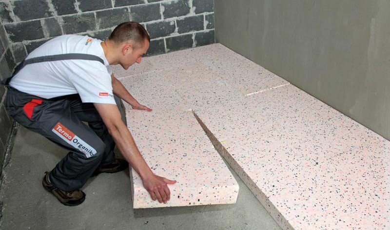 Zdjęcie przedstawia styropian ekspandowany (EPS). Widać robotnika, który nakłada go na podłogę. Styropian ma postać prostopadłościennych bloków, ma biały kolor.