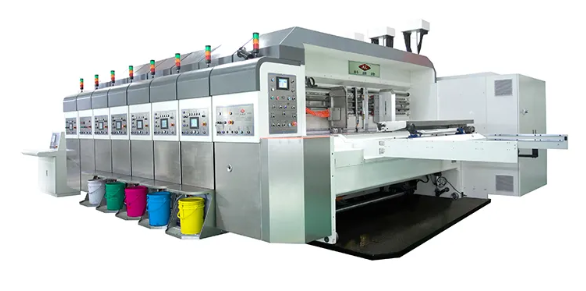 Na zdjęciu widać fleksograficzną maszynę drukującą; 4‑kolorową, z zespołem nakładającym lakier. Jest to duża maszyna. Na jej jednym boku znajduje się wiele przycisków. Pod nimi, na ziemi stoją kolorowe wiadra.