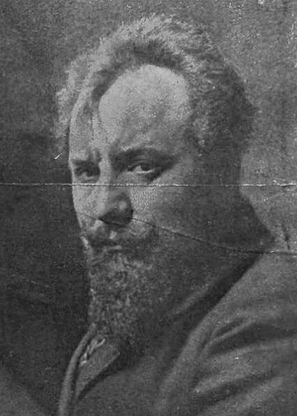 Zdjęcie przedstawia dojrzałego mężczyznę. Ma gęste, zwichrzone włosy i starannie przystrzyżoną brodę hiszpankę oraz wąsy. Ubrany jest w surdut.