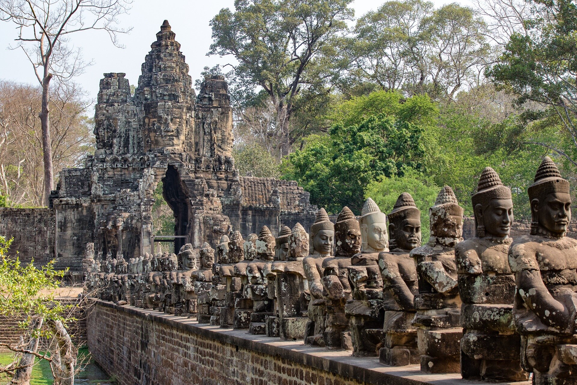 Fotografia przedstawiająca fragment Angkor Wat – największej, najważniejszej i najbardziej znanej świątyni w kompleksie Angkor, położonym w prowincji Siĕm Réab w Kambodży. Na barwnym zdjęciu widzimy rząd rzeźb o ludzkich kształtach oraz fragment budynku