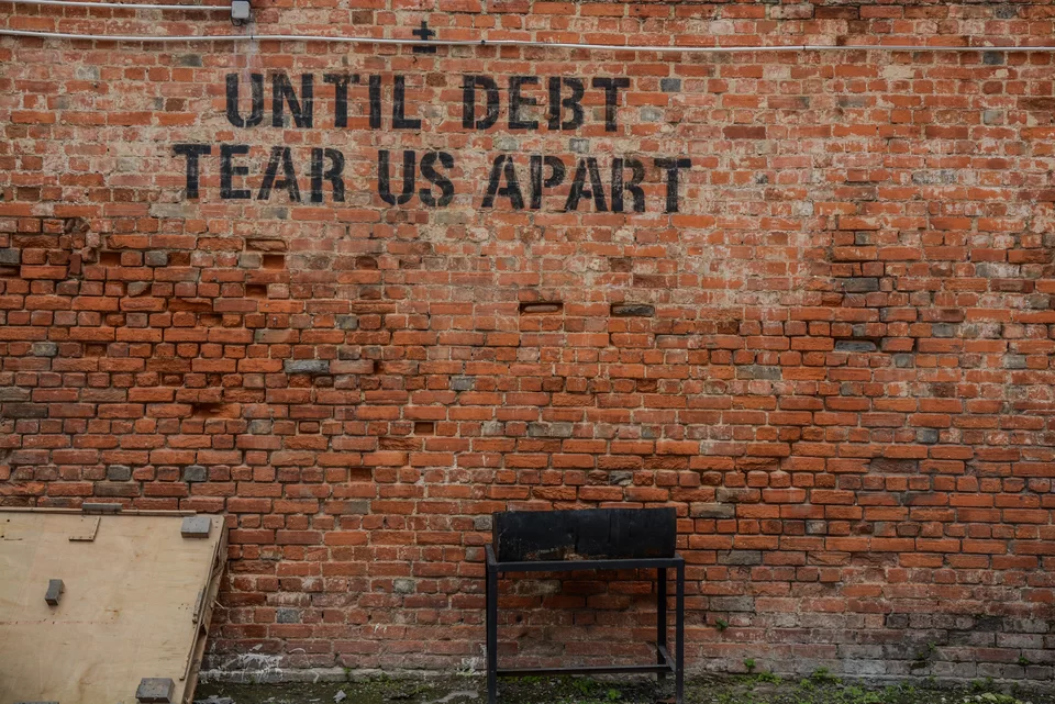 Zdjęcie przedstawia ceglaną ścianę, na ścianie napis w języku angielskim: Until debt tear us apart.