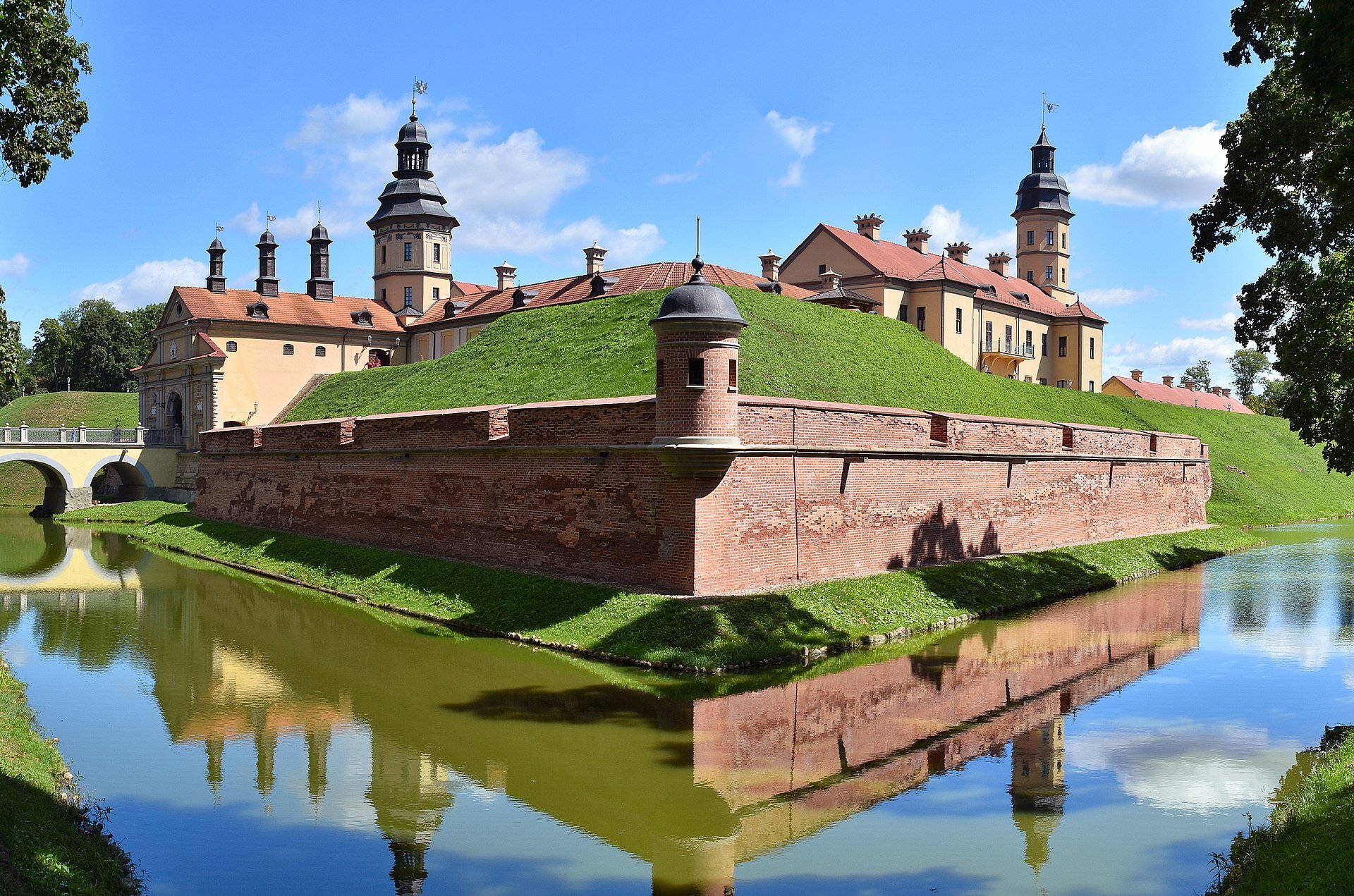 Na zdjęciu zamek położony na terenie otoczonym szeroką fosą. Na pierwszym planie grube mury obronne, dalej lekkie wniesienie, a na nim zabudowania zamkowe.