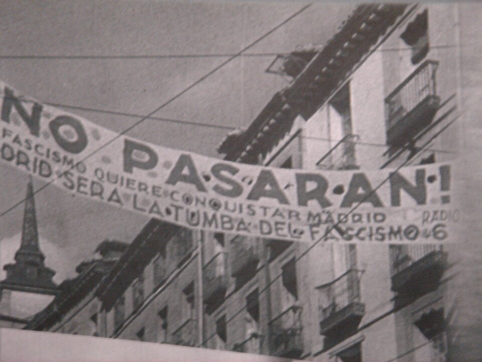 Zdjęcie przedstawia rozwieszony między budynkami baner z napisem No pasarán!