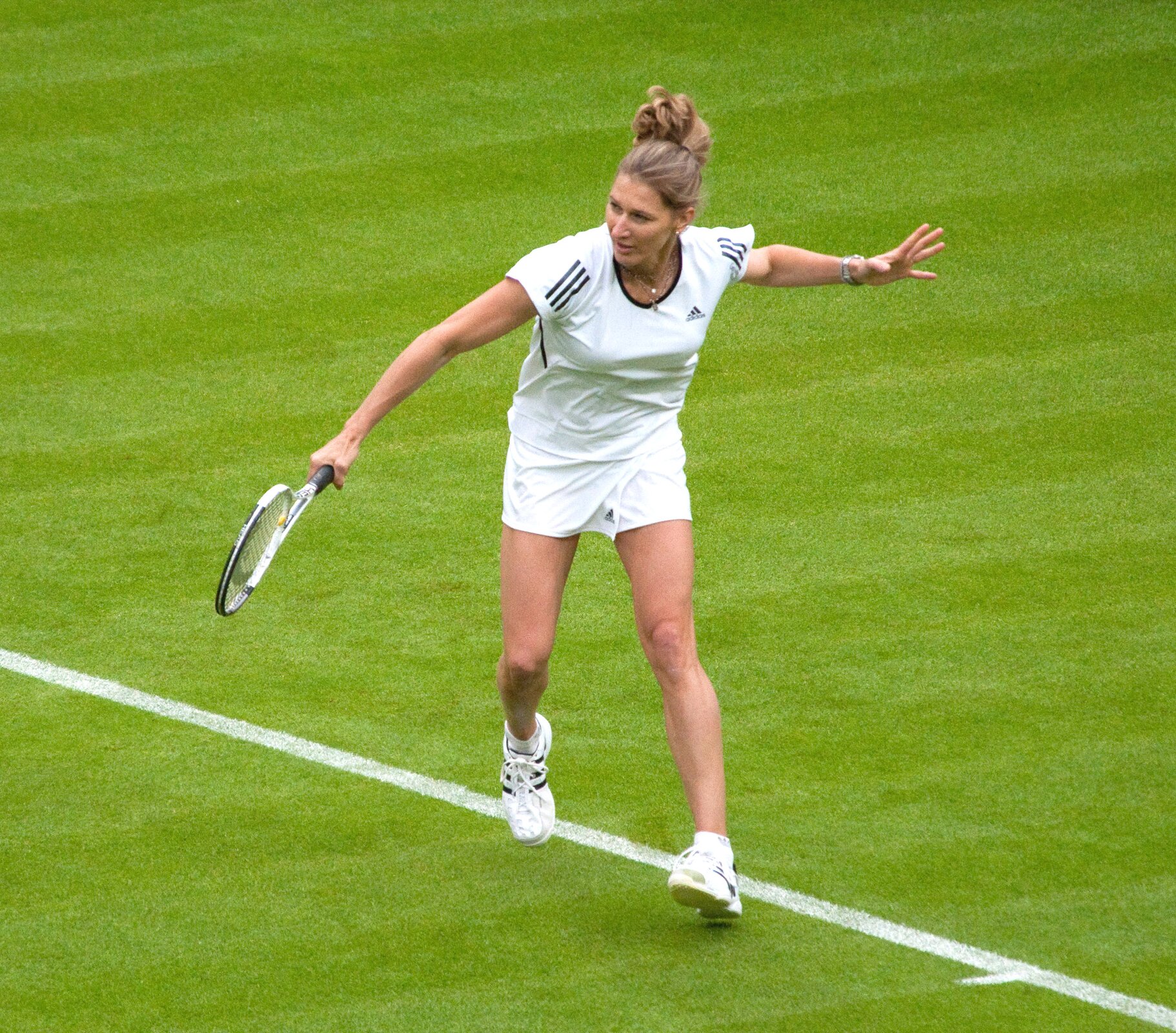 Ilustracja przedstawia tenisistkę w białych spodenkach i bluzce na zielonej murawie. W ręku trzyma rakietę gotową do odbicia piłki.