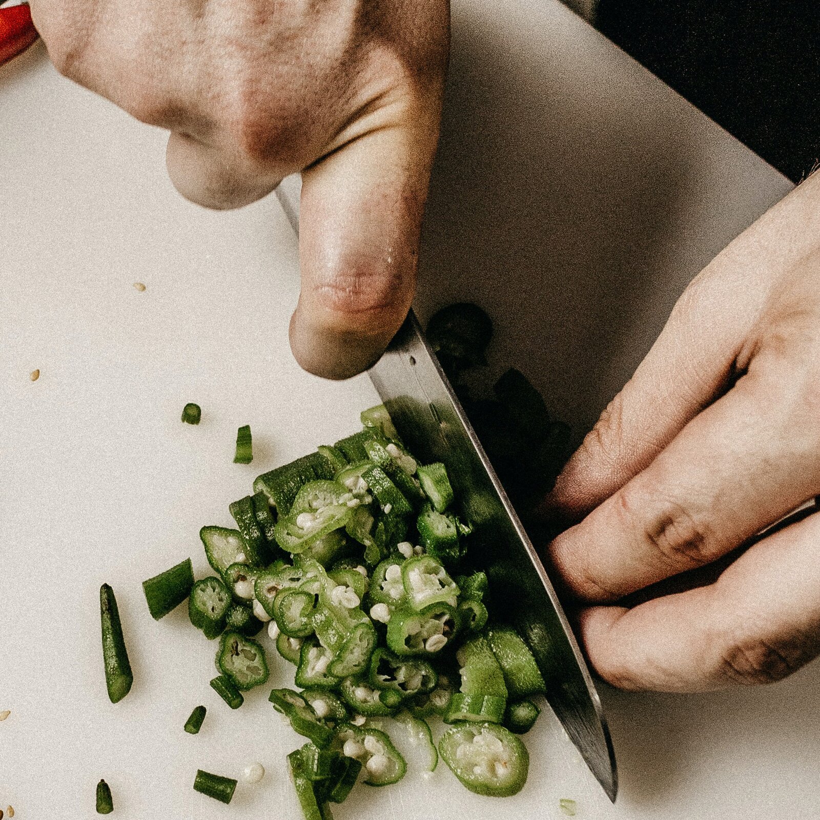 Zdjęcie przedstawia technikę trzymania podczas krojenia owoców i warzyw, tzw. uchwyt pazurowy. Z góry widoczne są dwie dłonie, z których prawa trzy metalowe ostrze noża, zawijając palec wskazujący na ostrzu, zaś prawa lekko zagięta, z palcami przyciśniętymi do siebie, przytrzymuje zieloną papryczkę. PO lewej stronie widoczne są poszatkowane talarki zielonej papryczki. Całość na tle wycinka prostokąta w kolorze kremowym, który obrazuje deskę do krojenia. 