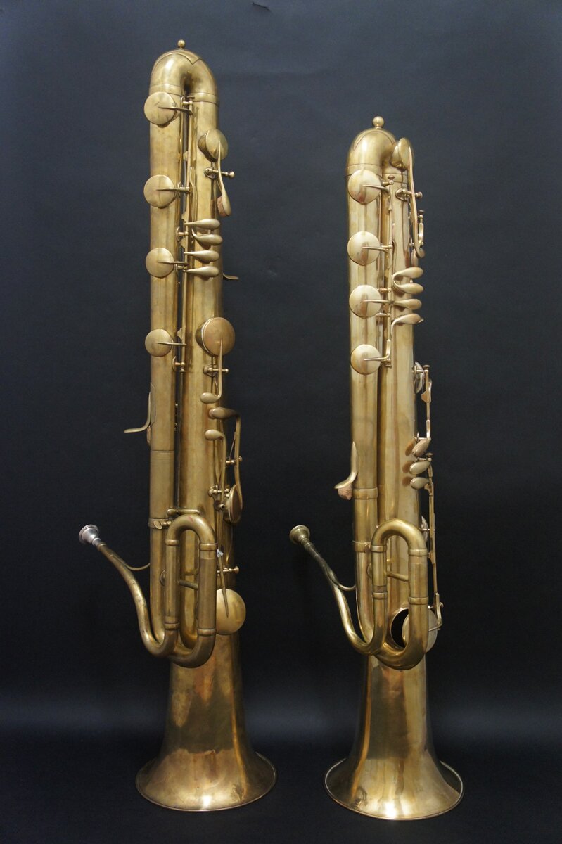 Ilustracja przedstawia dwa złote instrumenty (większy z lewej, mniejszy po prawej stronie), przypominające tubę. Mają złoty ustnik i liczne łukowate wygięcia korpusu, są zakończone szeroką czarą głosową.