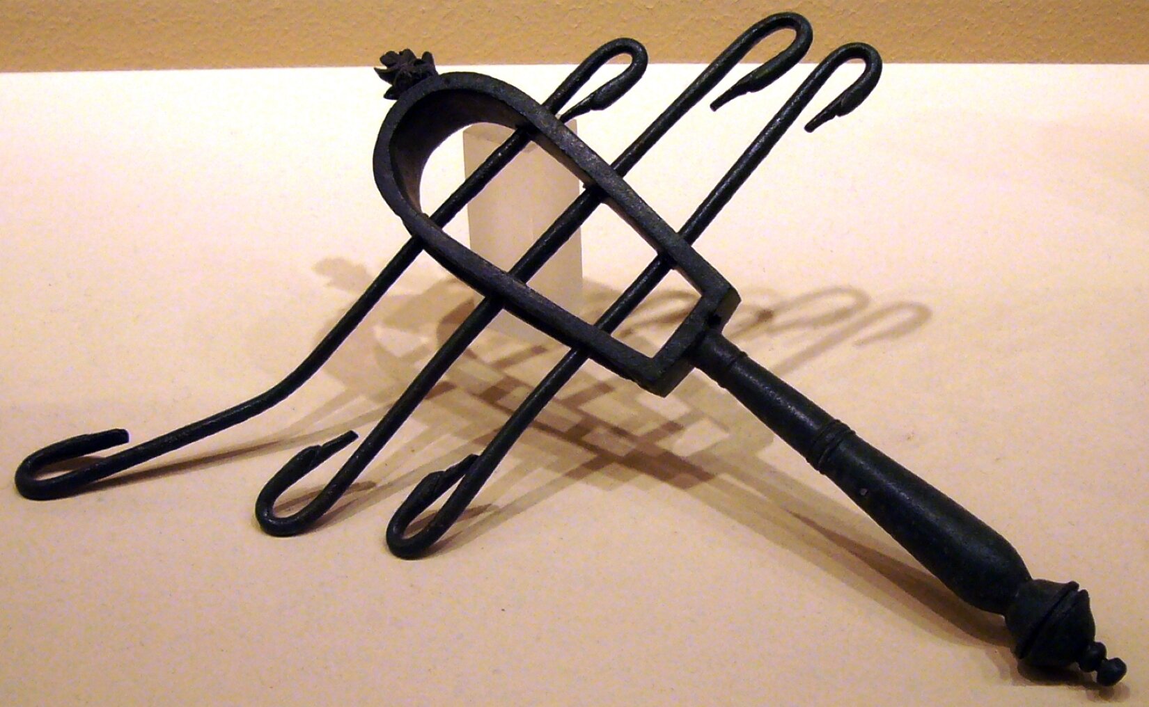 Na obrazie widoczny jest instrument o nazwie sistrum łukowe. Jest ono wykonane z brązu. Górna część instrumentu ma kształt bramy, przez które na różnych wysokościach przełożone są trzy metalowe pręty zagięte na obu końcach.