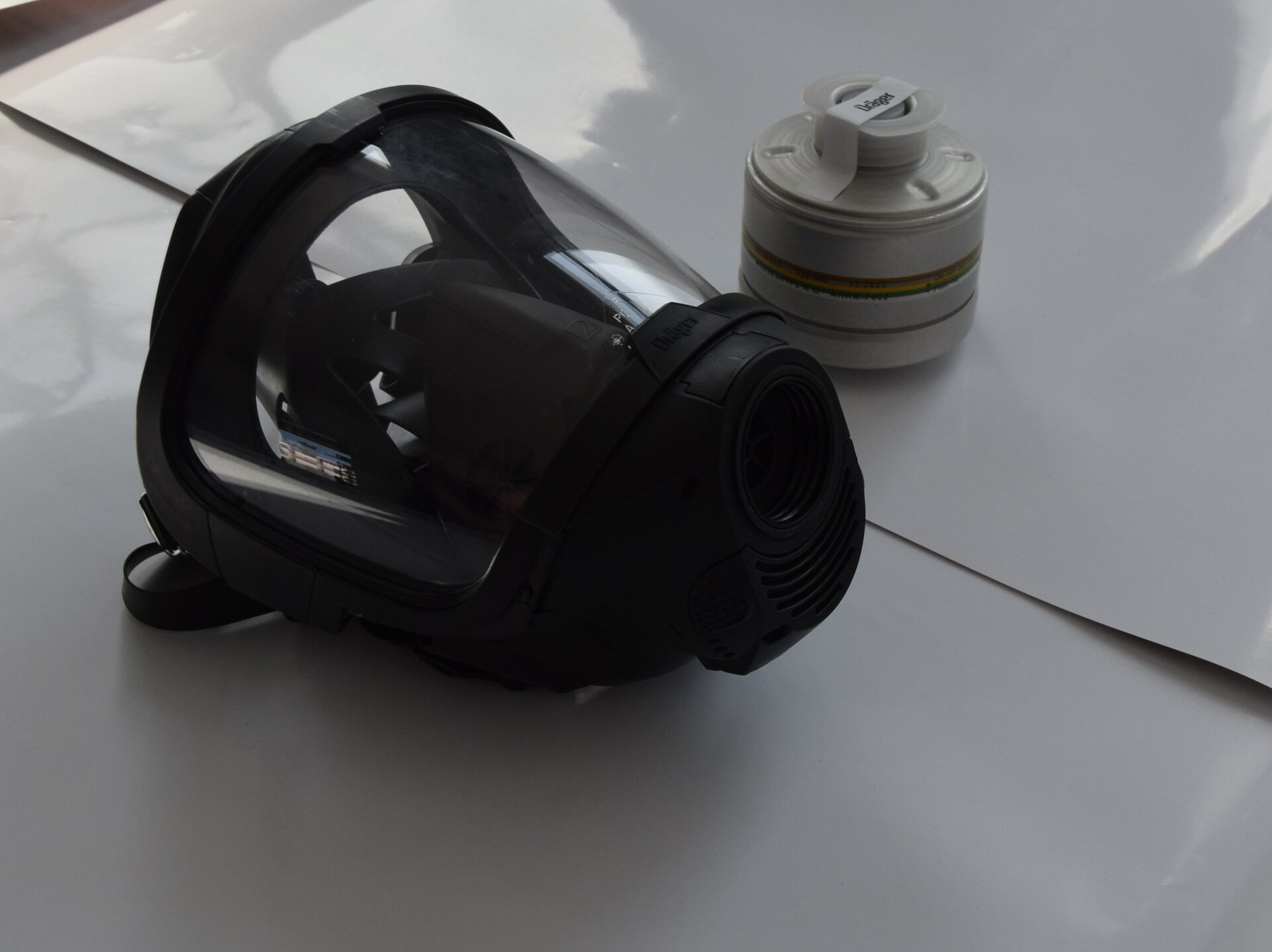 Na zdjęciu widoczna jest maska z pochłaniaczem. Maska jest w kształcie stożka. Powierzchnia boczna składa się z plastikowej szybki. Na dole maski widoczny jest otwór. Jest to otwór do którego montuje się pochłaniacz. Pochłaniacz leży z prawej strony maski. Pochłaniacz jest w kształcie grzybka.Poniżej zdjęcia w prawym dolnym rogu widoczny jest przycisk odtwarzania. Tekst nagrania jest zgodny z tytułem zdjęcia.