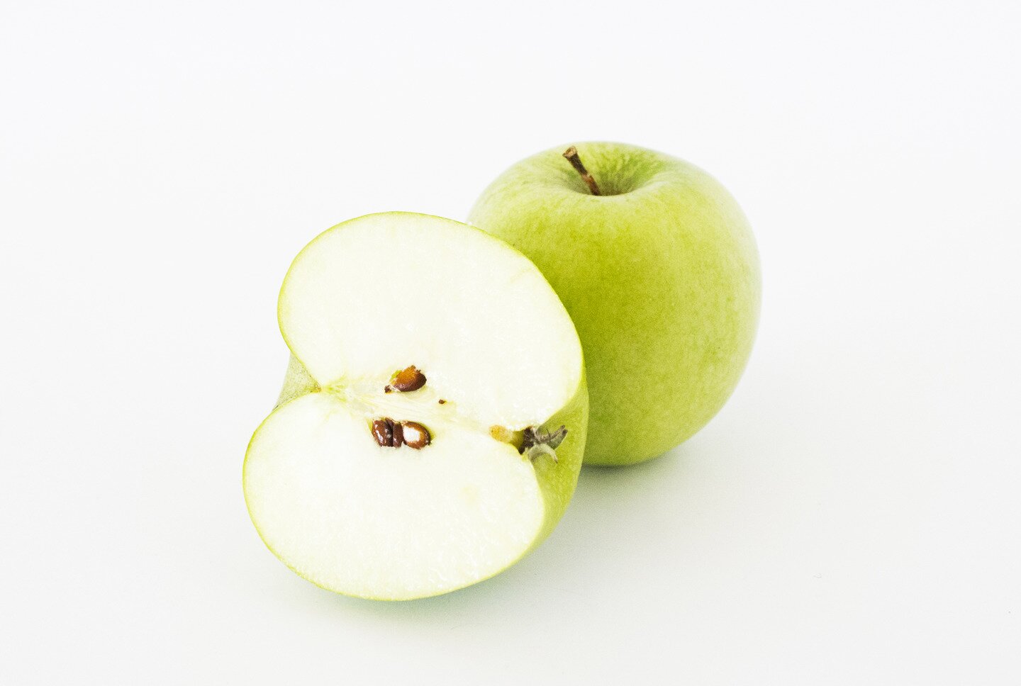 Fotografia przedstawia przekrojone wzdłuż jabłko, które jest oparte o położone  za nim drugie, całe jabłko. Środek przekrojonego jabłka ma komorę wypełnioną  małymi pestkami, widoczna jest również cienka skórka jabłka. Z drugiego jabłka wystaje krótki wąski, drewniany ogonek.