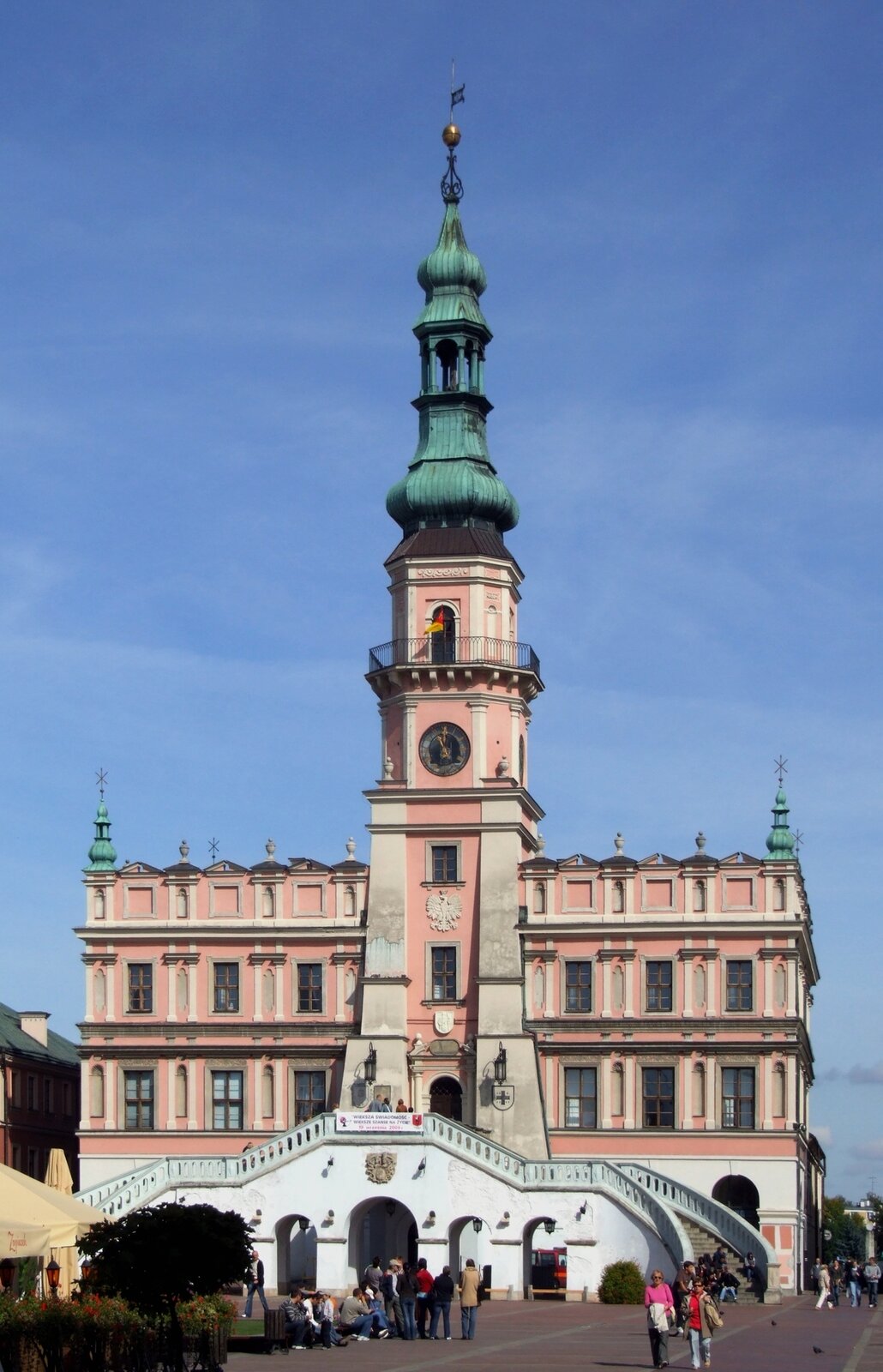 Ilustracja przedstawia ratusz w Zamościu. Ratusz posiada trzy kondygnacje (w projekcie Miranda miał tylko dwie). Główny korpus bryły założony jest na wysokim cokole. Pionową wieżę równoważą gzymsy. Do głównego wejścia prowadzą dwuramienne schody. Wejście główne dekorują: rzeźbiony kartusz kanclerski II ordynata Tomasza Zamojskiego z roku 1620 w przerwanym tympanonie, herb miasta ze Św. Tomaszem Apostołem, trzymającym tarczę z trzema włóczniami herbu Jelita rodu Zamoyskich oraz tarcza z Krzyżem Grunwaldu na prawej skarpie.