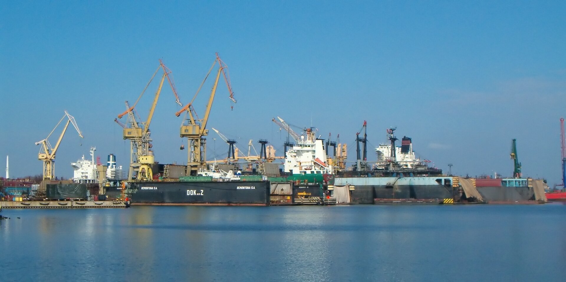 Na zdjęciu stocznia remontowa, liczne zabudowania portowe, dźwigi, kilka statków.