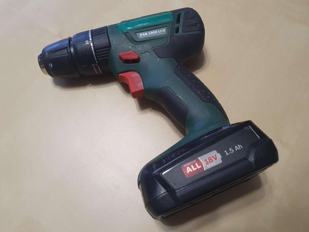 Zdjęcie przedstawia wiertarkę bezprzewodową. Składa się ona z akumulatora, rękojeści z przyciskami oraz głowicy do zamontowania wiertła. 
