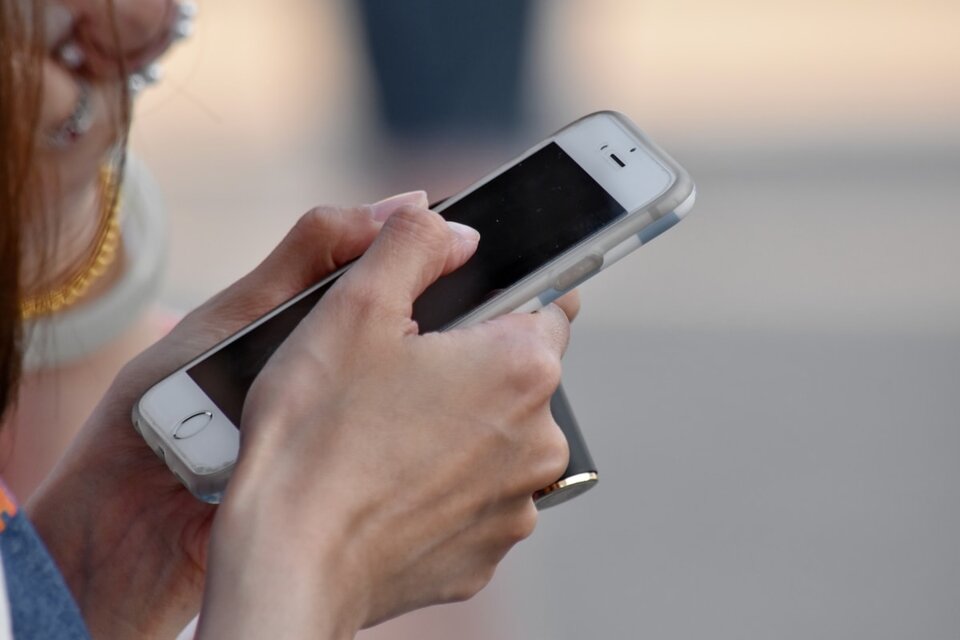 Kliknij aby powiększyć Ilustracja przedstawia kobiece dłonie trzymające smartfon w silikonowej obudowie, w kolorze białym z czarnym wyświetlaczem.