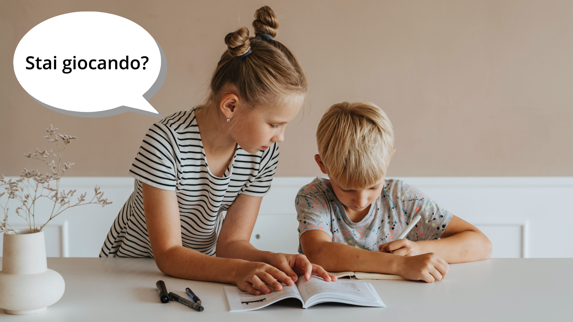 Zdjęcie przedstawia dziewczynkę i chłopca. Chłopiec znajduje się po prawej stronie i siedzi przy stole. Przed nim na blacie leży otwarta książka. Chłopiec coś pisze w zeszycie. Obok niego stoi, oparta łokciami o stół dziewczynka. Obok dziewczynki znajduje się dymek z pytaniem: Stai giocando?