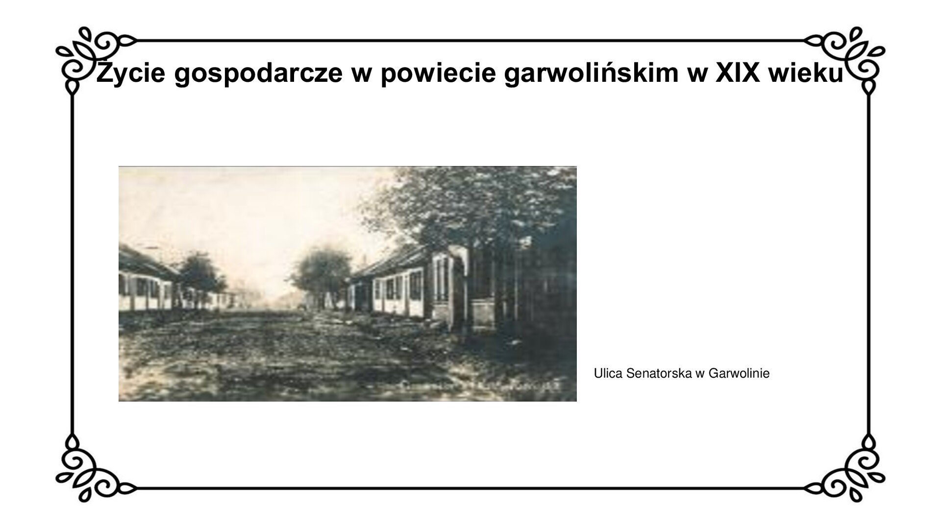kliknij, aby powiększyć Biały slajd. U góry nagłówek: „Życie gospodarcze w powiecie garwolińskim w XIX wieku”. Niżej, z lewej strony slajdu, zdjęcie przedstawiające wybrukowaną ulicę z rynsztokami i chodnikami dla pieszych, biegnącą przez jego środek. Przy chodnikach zasadzone są drzewa. Budynki przy ulicy są drewniane, parterowe, a znajdujący się po prawej stronie fotografii ma ganek. Okna w budynkach mają okiennice, a dachy są dwuspadowe. Obok zdjęcia podpis: „ Ulica Senatorska w Garwolinie”.