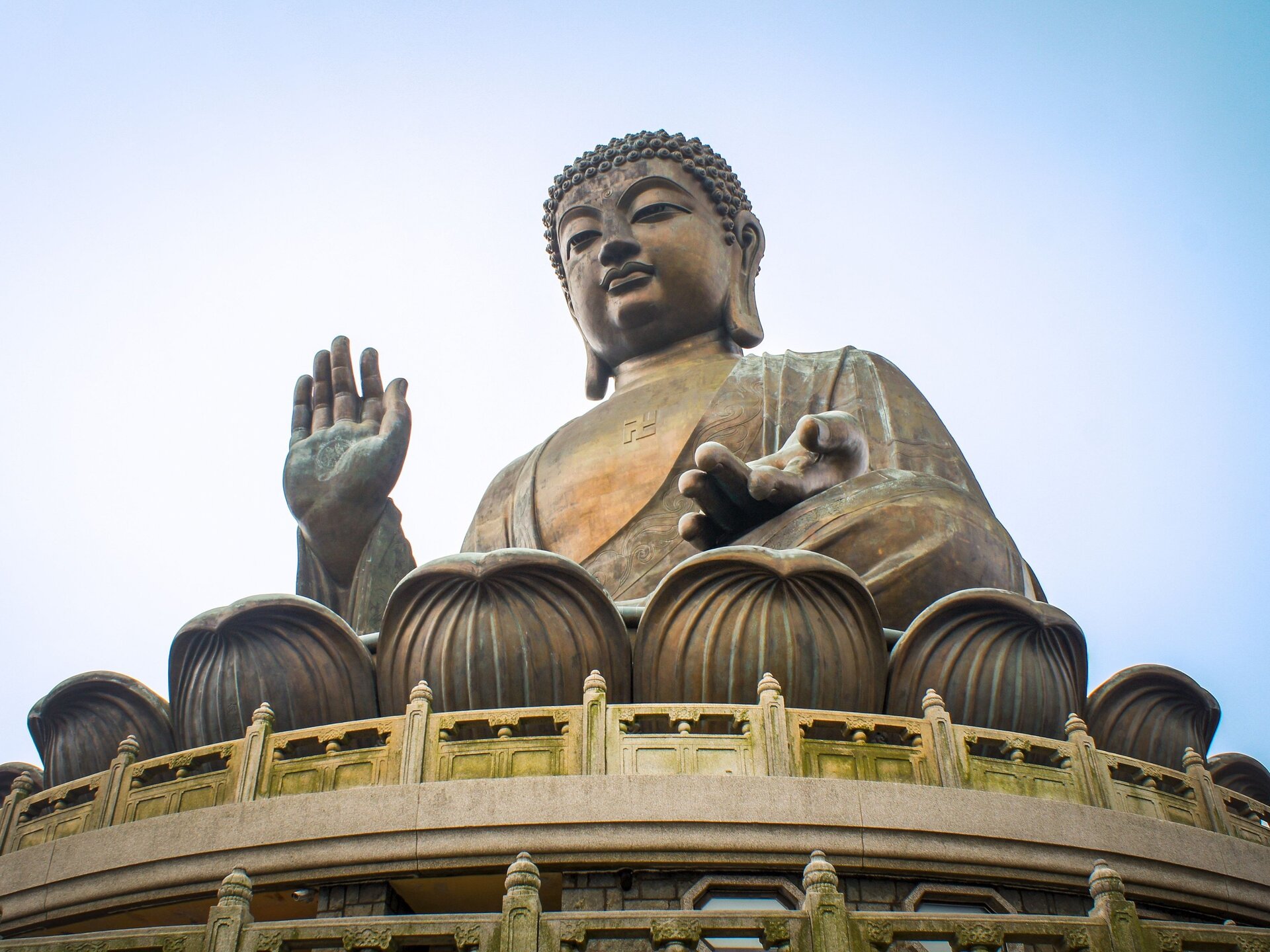 Kamienny posąg Buddy. Siedzi ze skrzyżowanymi nogami. Jedną dłoń opiera wierzchem na kolanie, drugą unosi lekko w górę. Ma otwarte oczy.