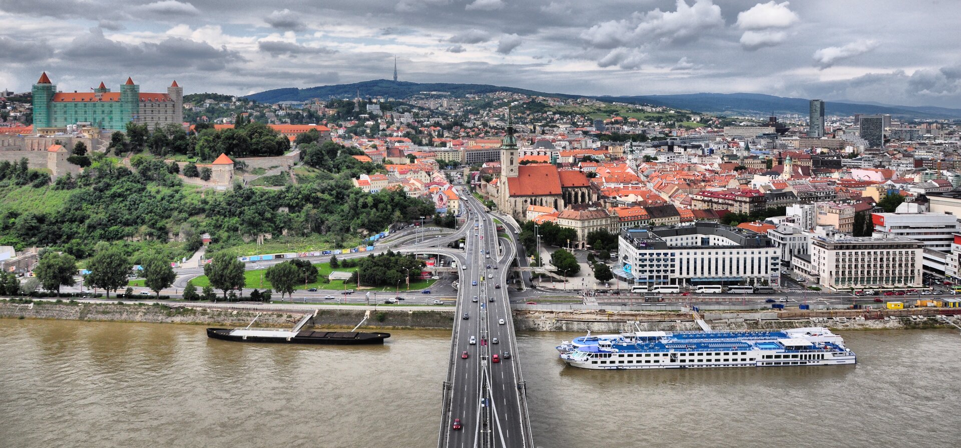 Widok z lotu ptaka na Stare Miasto w Bratysławie. Na pierwszym planie most, rzeka, statek wycieczkowy.