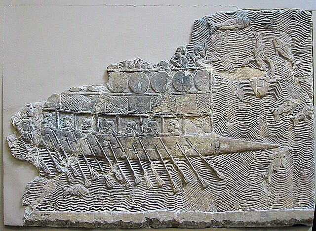 Zdjęcie przedstawia fragment reliefu. Jest na nim ukazana galera z jednym rzędem wioseł. Powyżej pokładu galerników widać kolejny pokład, na którym znajdują się żołnierze.
