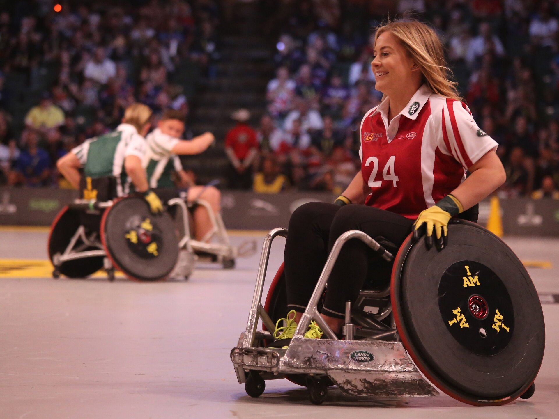 Widoczne są osoby na wózkach przystosowanych do uprawiania sportu. Znajdują się na boisku. Mają na sobie sportowe stroje.
