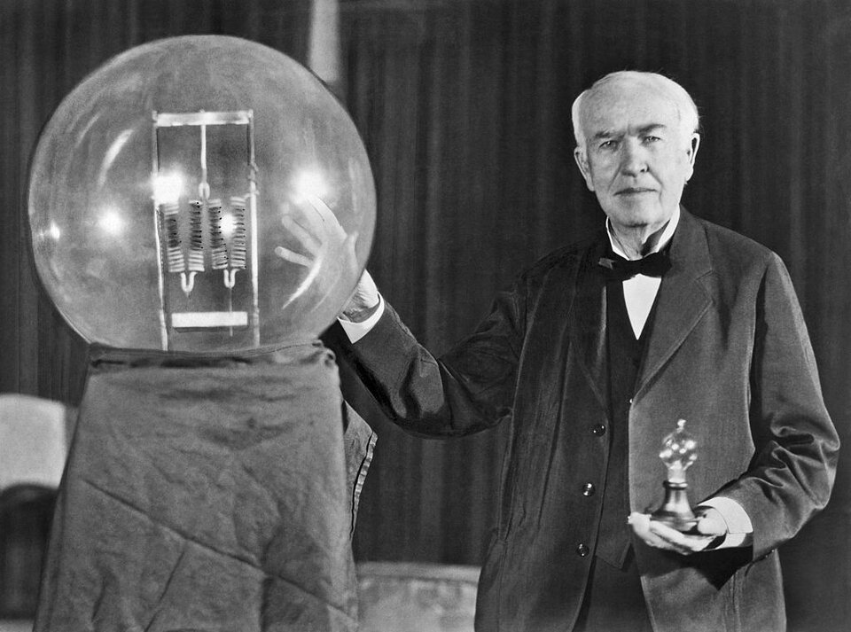 Na ilustracji przedstawiony jest Thomas Edison, uznawany za twórcę żarówki. Po prawej stronie stoi starszy mężczyzna w czarnym garniturze i białej koszuli, z zawiązaną pod szyją muszką. Prawą rękę położył na dużej szklanej kuli umieszczonej na ciemnym postumencie. W lewej dłoni trzyma niewielką figurkę. Mężczyzna stoi zwrócony twarzą do oglądających. Tło stanowi czarna kotara. 