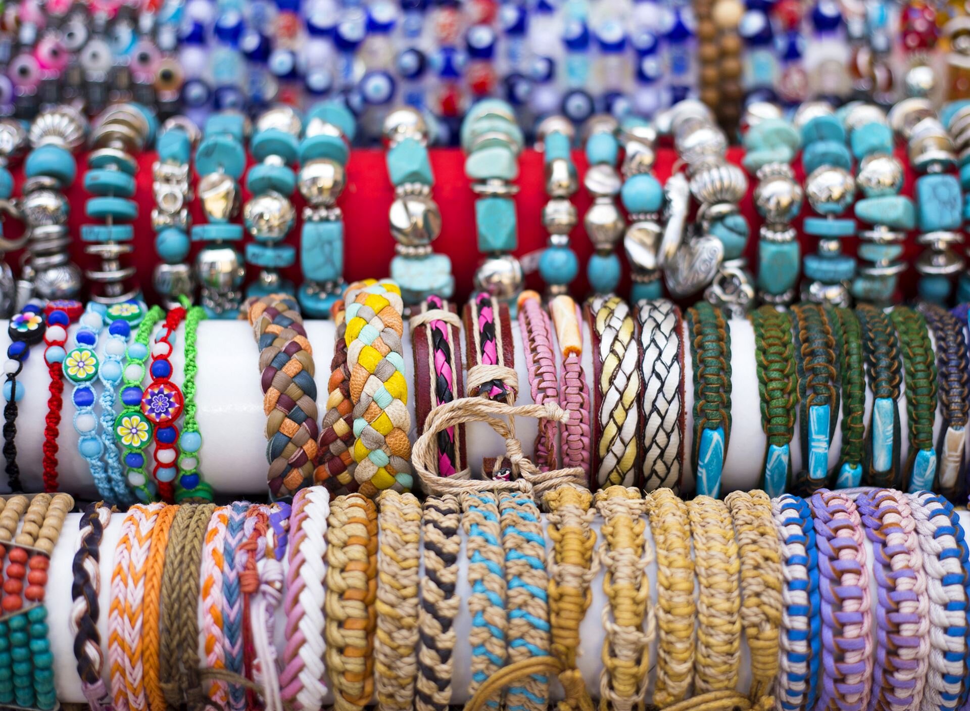 Kolorowe zdjęcie przedstawia cztery rzędy ręcznie robionych bransoletek, wykonanych z różnokolorowej włóczki, sznurka, rzemyków i nitek. Ozdobiono je kamieniami szlachetnymi, koralikami o różnych kształtach i kolorach.