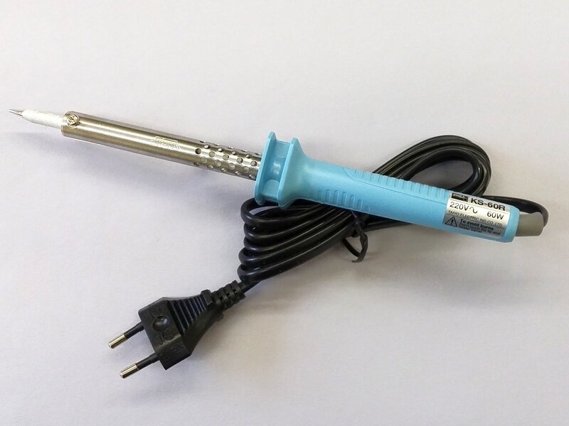 Zdjecie przedstawia lutownicę, która wyglądem przypomina długopis z przeciwnej strony wystaje kabel. Połowa lutownicy jest plastikowa z naklejką 220 zmienny prąd 60 W. Druga połowa jest metalowa zakończona ostrym wierzchołkiem.