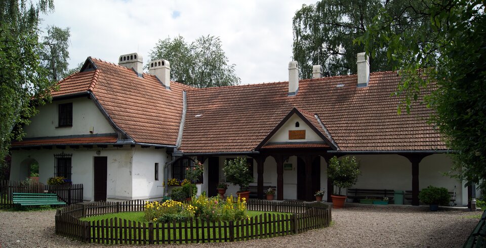 Na zdjęciu znajduje się zabytkowy dwór Rydlówka. Parterowy budynek jest zbudowany na planie prostokąta. Przylegające skrzydło posiada piętro. Dach jest pokryty dachówką. Budynek ma alkierz wsparty na czterech drewnianych ozdobionych słupach. Przed dworkiem znajduje się kolista rabata z kwiatami, otoczona drewnianym płotkiem. 