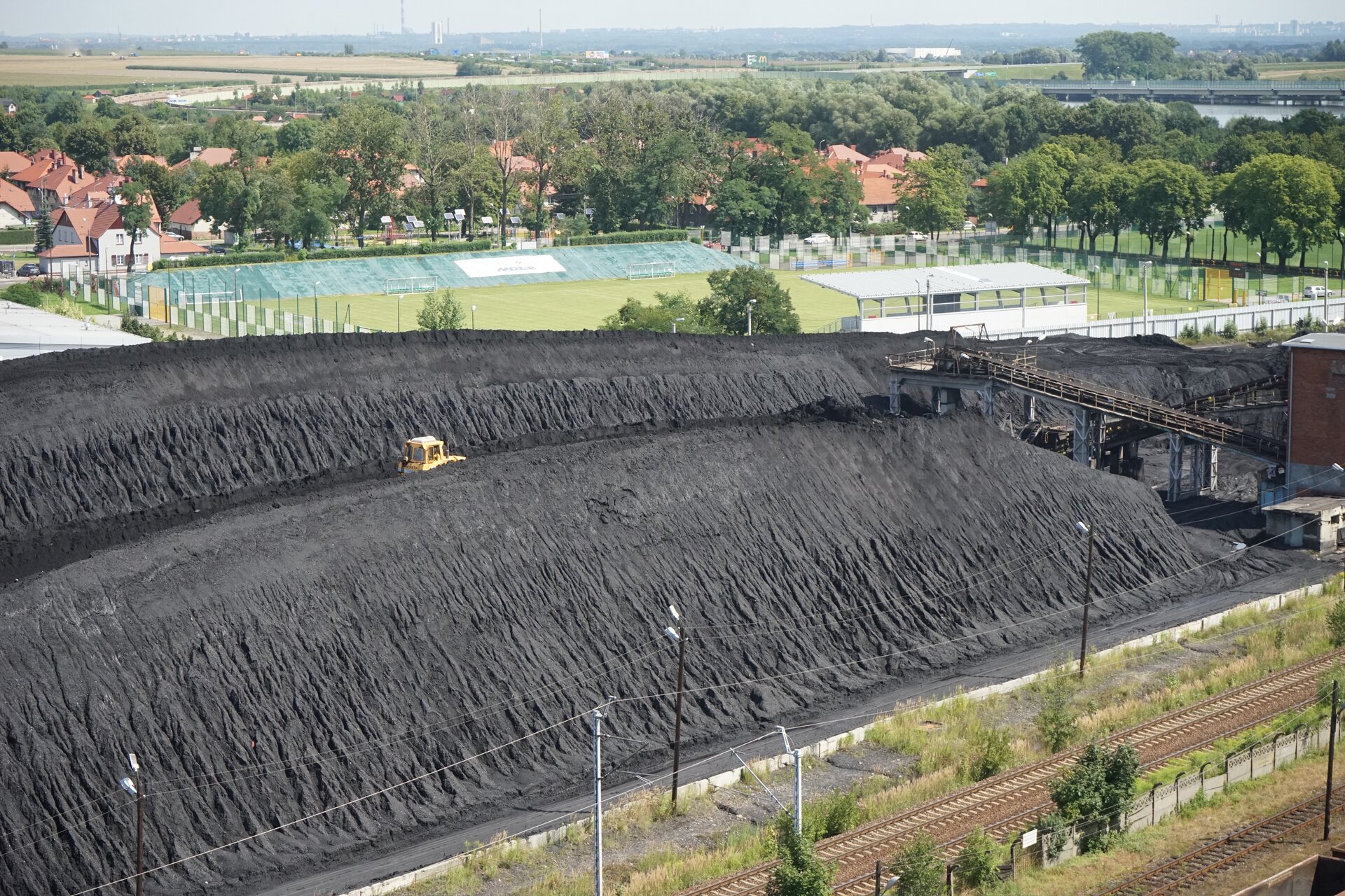 Na zdjęciu widoczne są zwałowiska węgla kształtowane przy pomocy ciężkiego sprzętu. W centralnej części ekranu widać dwa duże zwałowiska o kształcie graniastosłupa o podstawie trójkąta. Pomiędzy zwałami widoczna jest duża żółta spycharka. Po prawej stronie zwałowiska biegną tory. W górnej części zwałowiska widoczny jest przenośnik taśmowy.Poniżej zdjęcia widoczny jest przycisk multimedialny z nagraniem audio. Treść nagrania jest zgodna z tytułem zdjęcia.