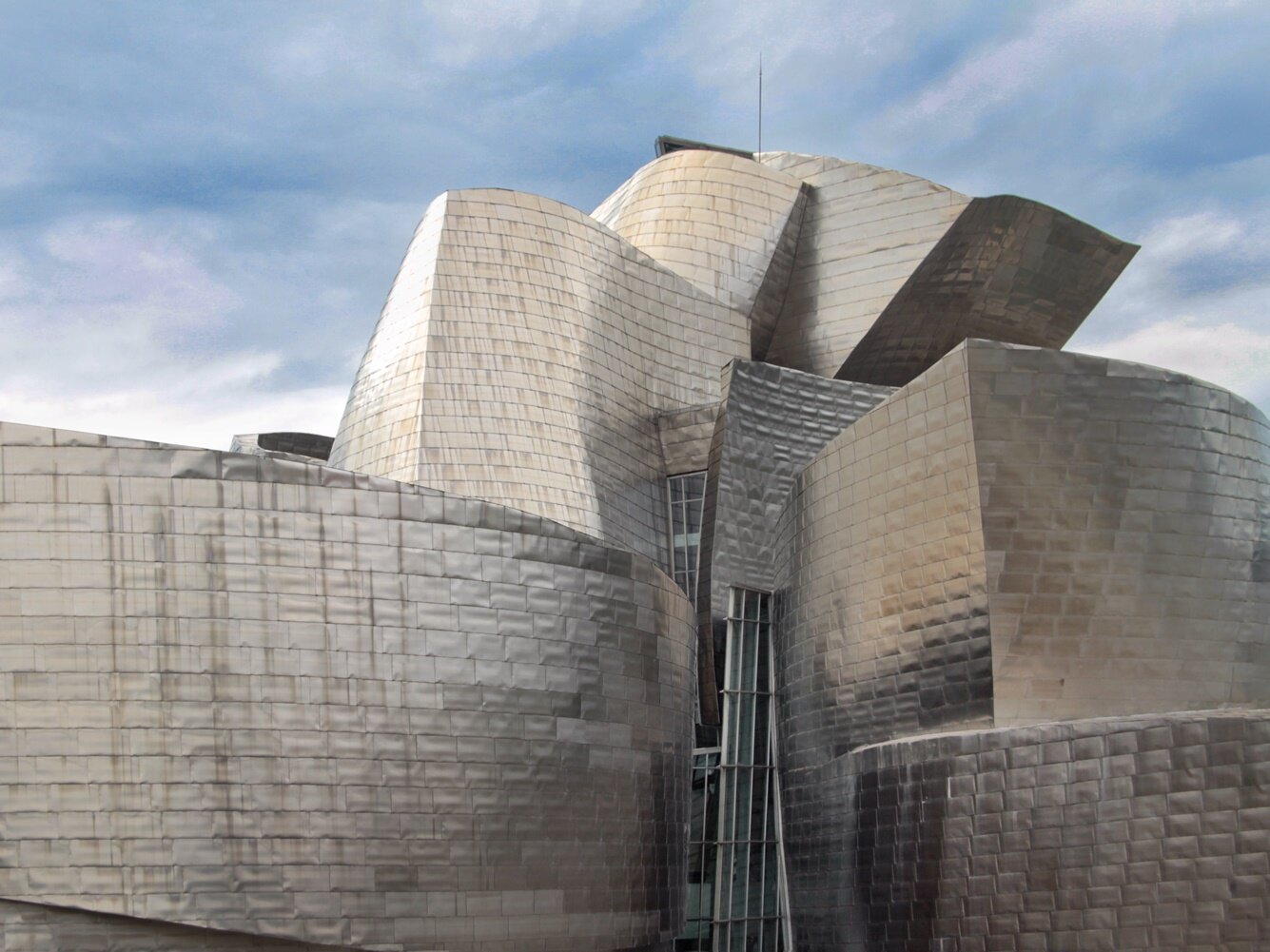 Zdjęcie przedstawia supernowoczesny budynek, o futurystycznym kształcie, którego dach przypomina powyginane fale wykonane ze srebrnej blachy.