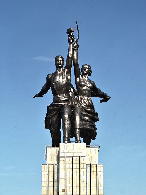 Zdjęcie przedstawia pomnik. Na wysokim postumencie stoi para: po lewej stronie widać robotnika z młotem w lewej ręce, po prawej robotnicę z kołchozu z sierpem w prawej dłonidłoni. 