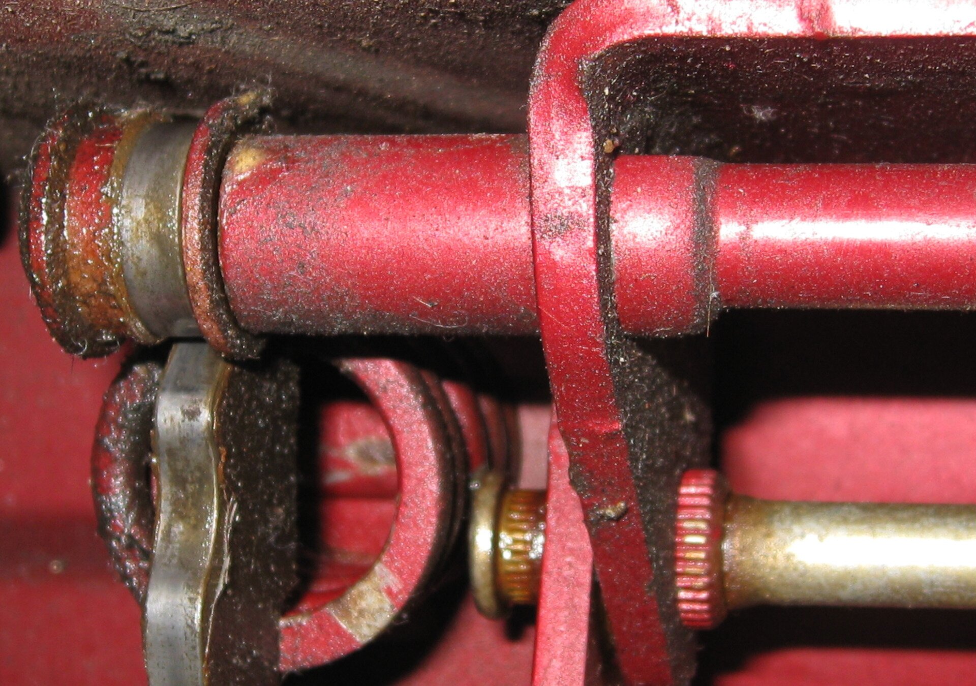 Fotografia przedstawia czerwone rurki jakiejś maszyny pobrudzone smarem.