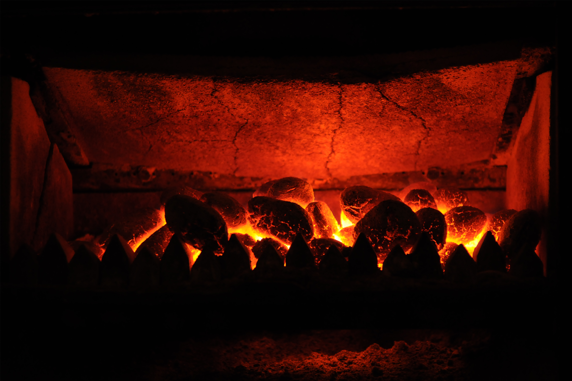 Zdjęcie przedstawia rozżarzone kawałki węgla palącego się w piecu czerwonym płomieniem.