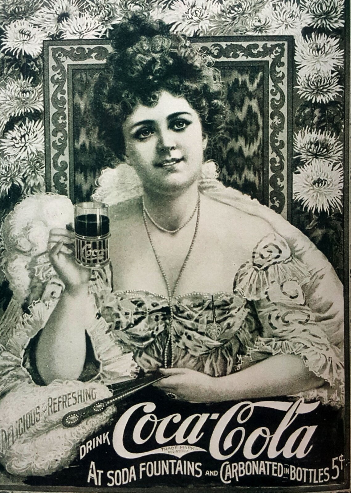 Fotografia przedstawiająca plakat reklamujący coca-colę z początku XX wieku. Kobieta w koku i eleganckiej sukience trzyma w prawej dłoni filiżankę od herbaty, w której znajduje się napój coca-cola. W dole ilustracji widnieje napis "Drink Coca-cola at soda fountains and carbonated in bottles". Zdjęcie jest czarno - białe.