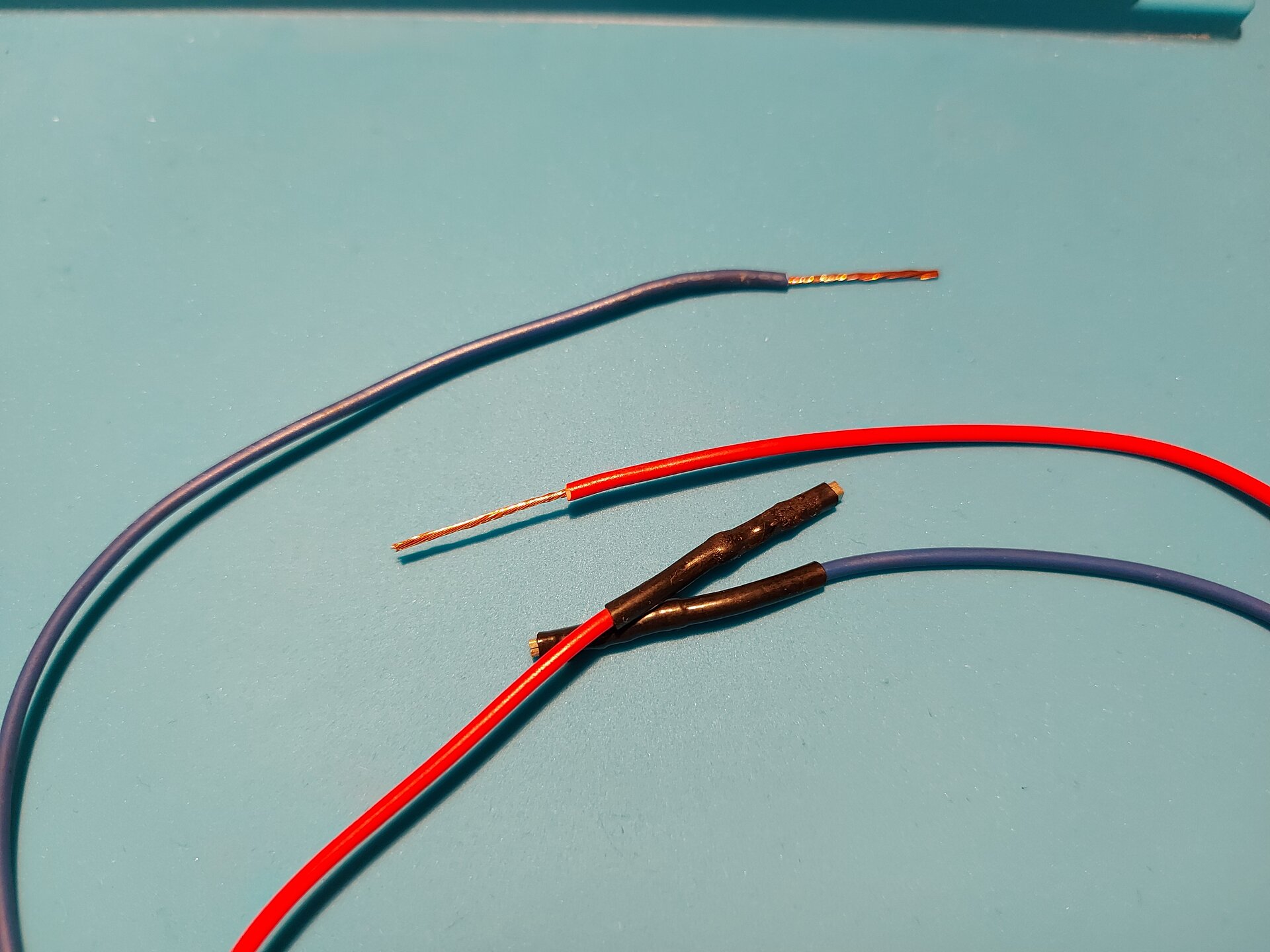 Zdjęcie przedstawia 4 przewody z czego 2 z usuniętą izolacją tym samym odsłaniając miedziane wnętrze, pozostałe zostały osłonięte taśmą izolacyjną.