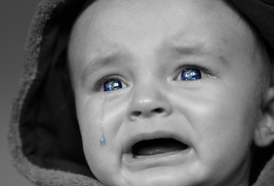 Fotografia czarno-biała przedstawia małe dziecko płaczące i patrzące w dal.