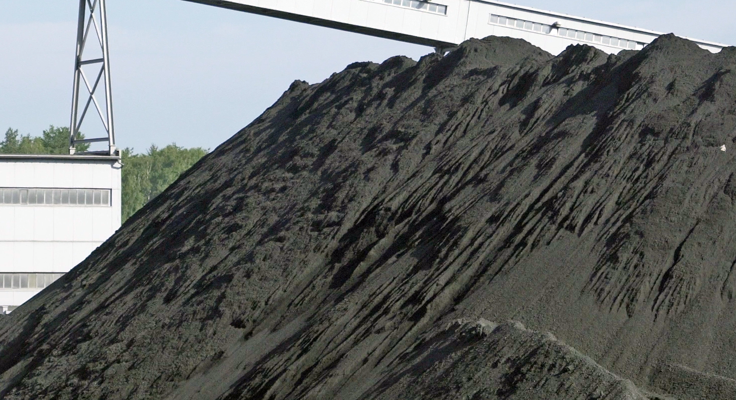 Na zdjęciu widać hałdę węgla. Węgiel jest składowany w formie pryzmy. Widoczny węgiel ma małe rozmiary ziarna. W tle widać zapadający łącznik o kształcie prostopadłościanu.
