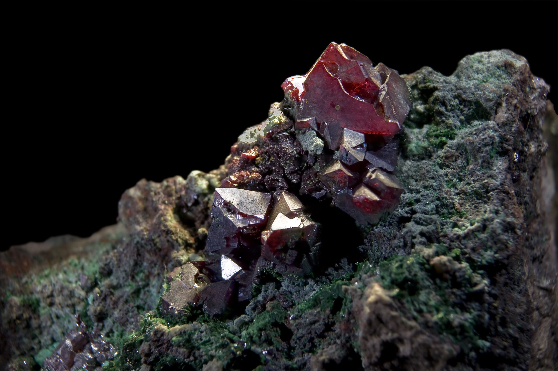 Na zdjęciu na fragmencie szarej skały są czerwone kryształy.