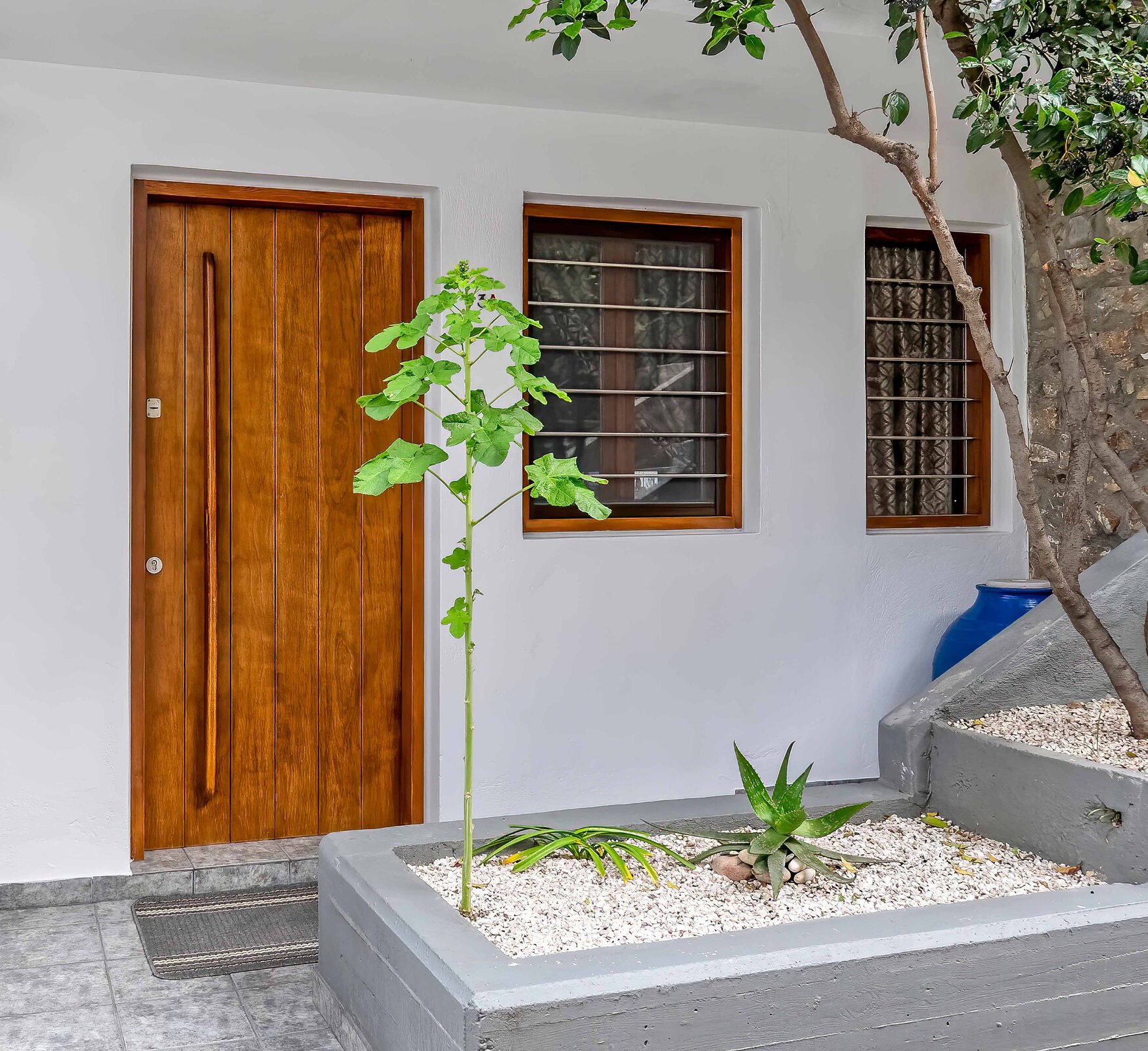 Zdjęcie przedstawia drewniane drzwi zewnętrzne bez klamki, wyglądające tak, jakby były złożone z kilku pionowo ułożonych paneli drewnianych.