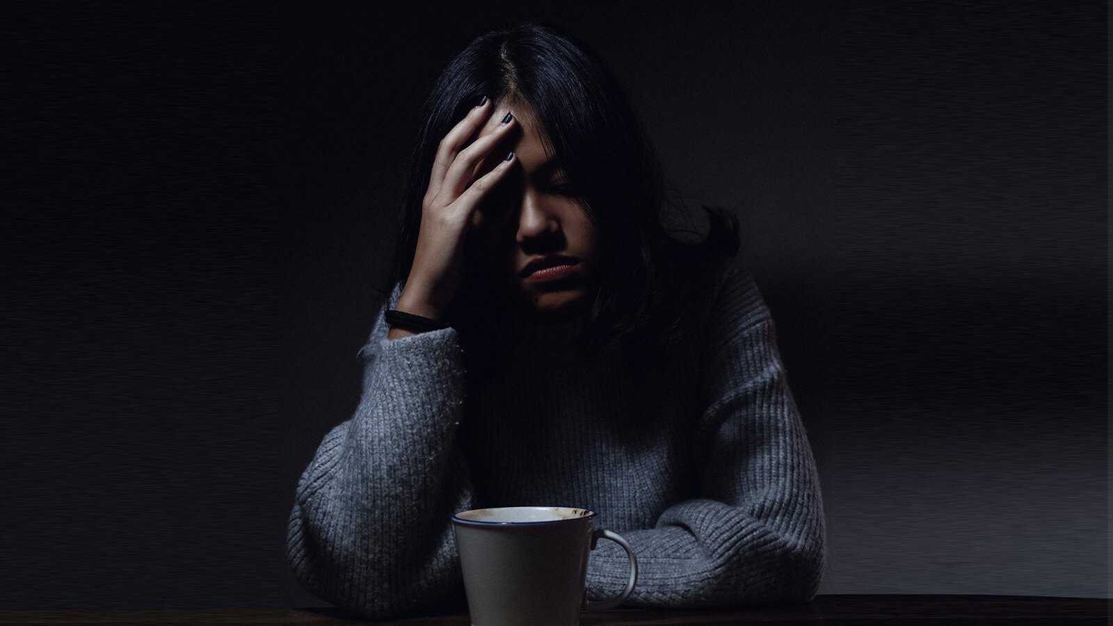 Zdjęcie przedstawia młodą kobietę opierającą głowę na prawej dłoni. Kobieta ma smutny wyraz twarzy. 