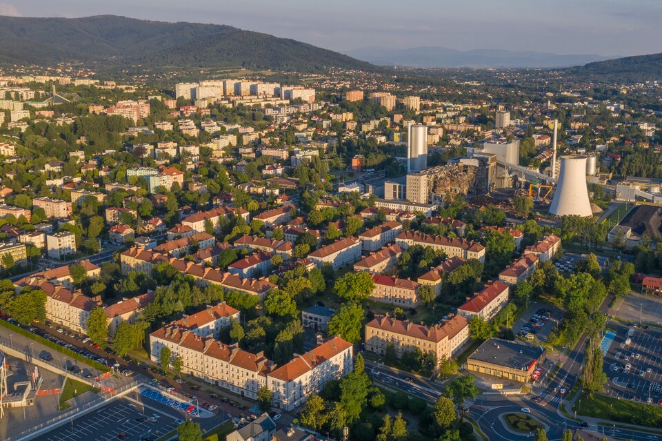 Zdjęcie przedstawia panoramę miasta z lotu ptaka. Na pierwszym planie znajduje się osiedle złożone z bloków mieszkalnych. Pomiędzy nimi znajdują się liczne drzewa.
