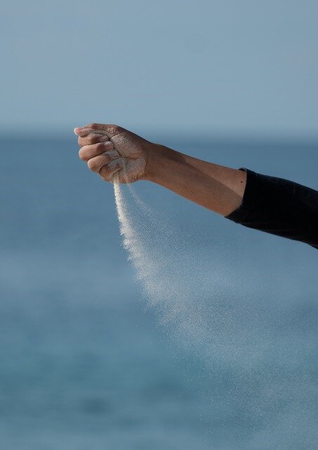 Zdjęcie przedstawia ludzką dłoń zaciśniętą w pięść. Z dłoni sypie się biały, drobny popiół.